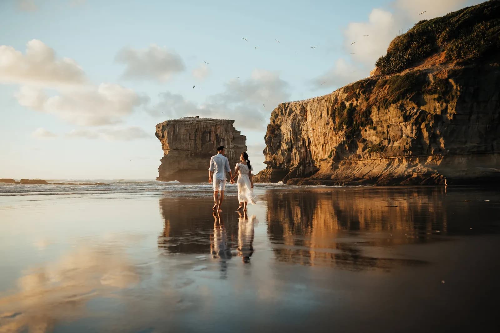 Couple walking on a beach at sunset near sea cliffs, captured by V Visual