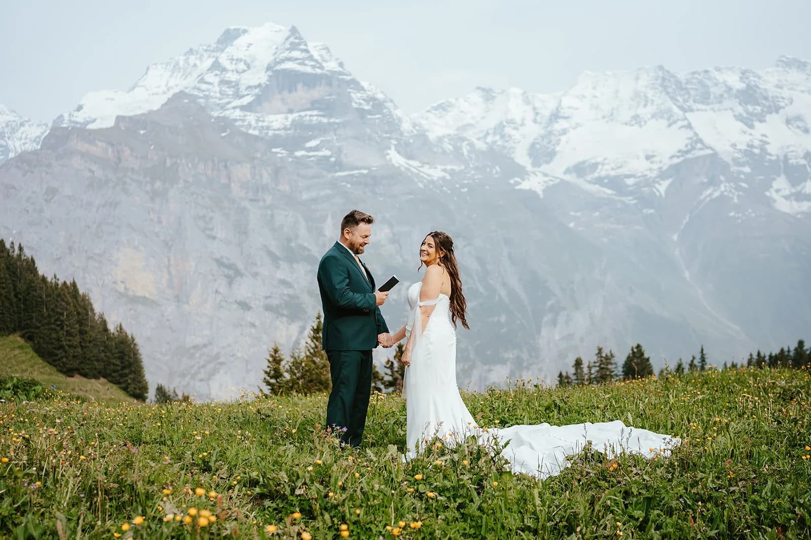 Couple exchanging vows in an alpine meadow with snow-capped mountains behind them